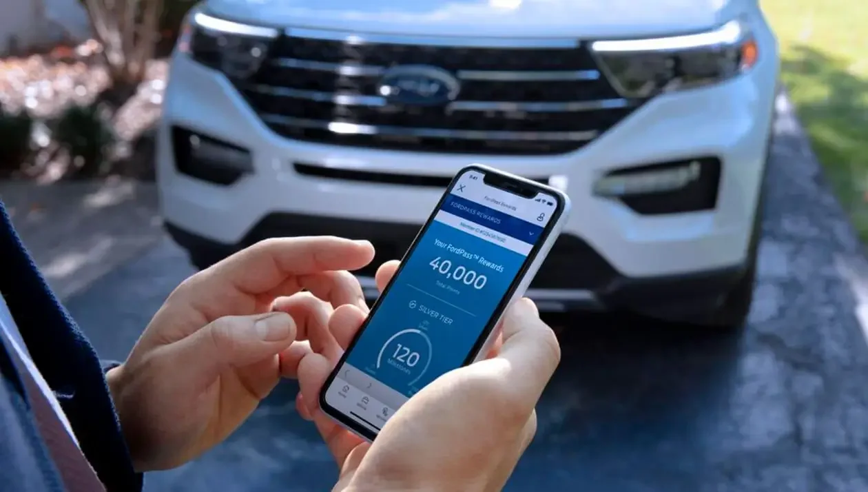 Closeup of a cell phone in a man's hand scheduling service in font of white Explorer® SUV