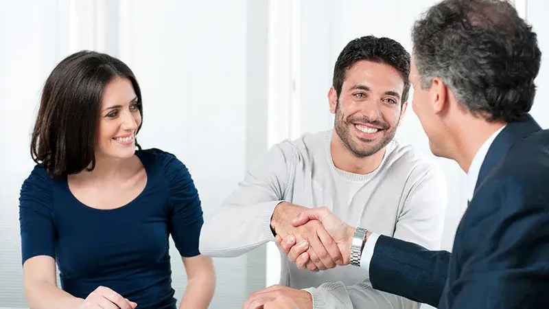 A salesperson shaking the hand of a man sitting next to a woman