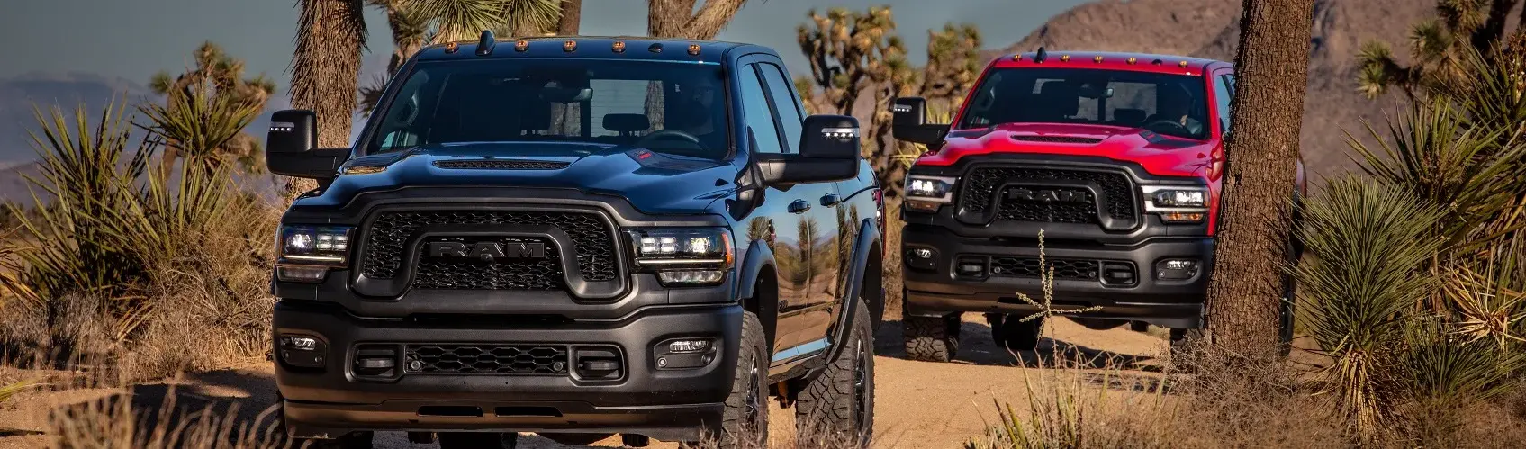 Two Ram trucks driving down a dirt road