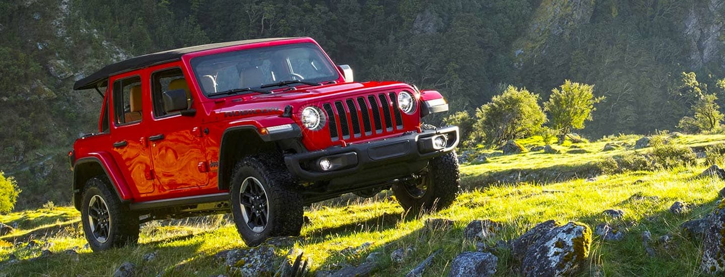 2019 Jeep Wrangler Rubicon exterior shot with red paint color driving on rocky mountain terrain near a creek