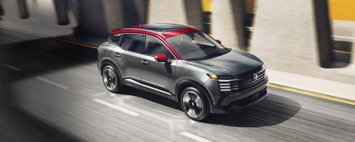 A gray Nissan Kicks with a red roof driving quickly down the highway.