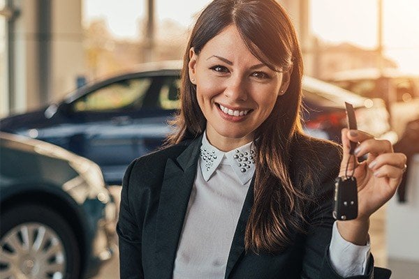 Cheerful young woman showing her new car key at dealership.