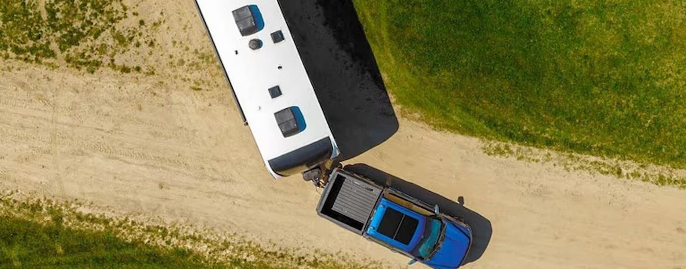 Blue 2025 Ford F-150 XLT towing a trailer on a dirt road