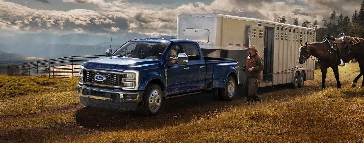A blue 2026 Ford F-350 for sale from the side towing a trailer.