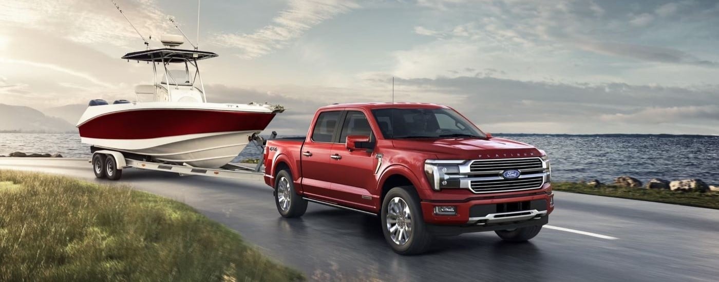 Red 2024 Ford F-150 Platinum Plus towing a boat past a lake