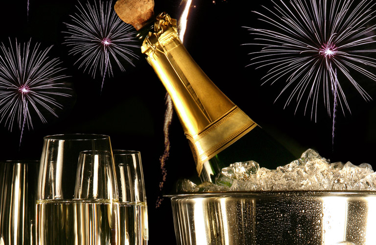 opening a bottle of champagne with multiple glasses and a bucket of ice, fireworks in the background